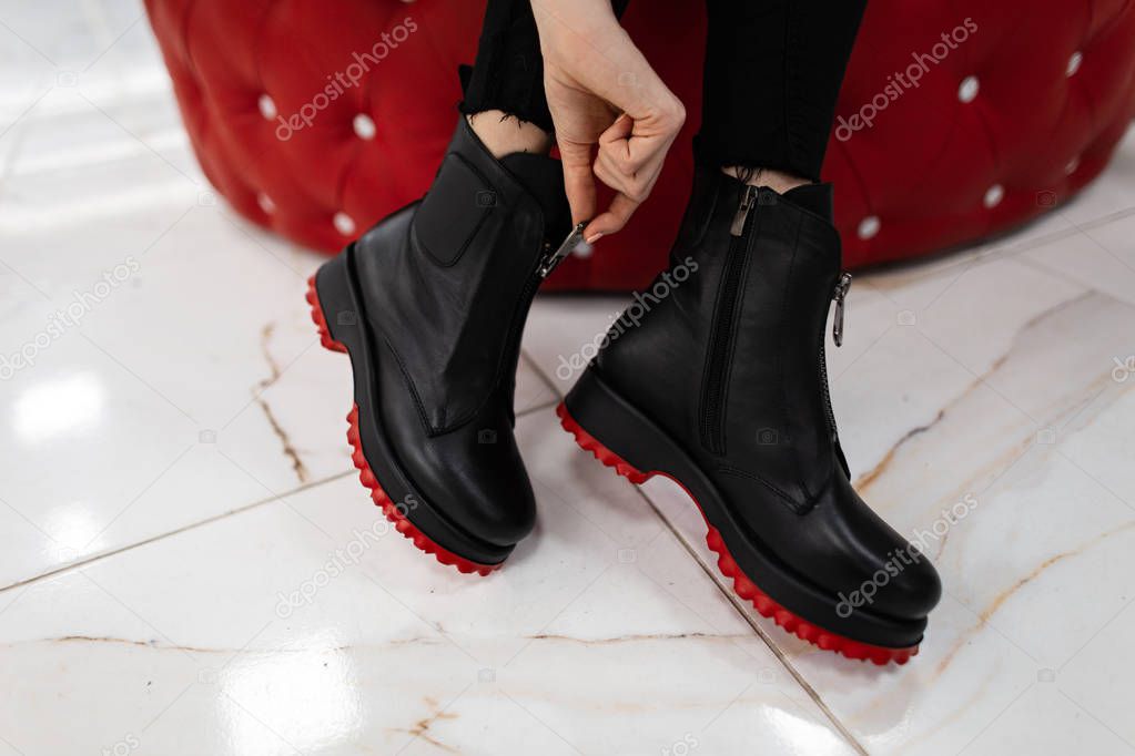 Fashionable woman sits in a store and measures autumn shoes.Close-up of female legs in stylish jeans in trendy leather black boots with red soles. New seasonal collection of women's footwear.