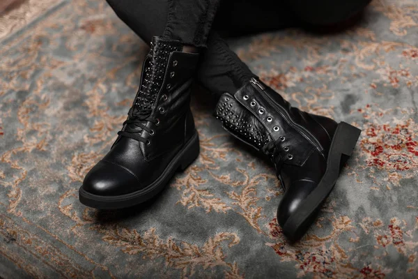 Divatos fiatal nő ül egy vintage padlón egy boltban fekete elegáns bőr cipő fűzés farmer. Női lábak közelsége divatos őszi tavaszi csizmában. Új stílusos cipőkollekció — Stock Fotó