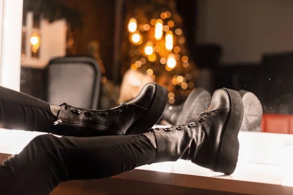 Stijlvolle jeugd lederen zwarte laarzen op vrouwelijke benen. Close-up van vrouwelijke benen in jeans in modieuze schoenen in de buurt van een vintage spiegel met heldere lampen. Meisje kiest schoenen voor een feestje. — Stockfoto