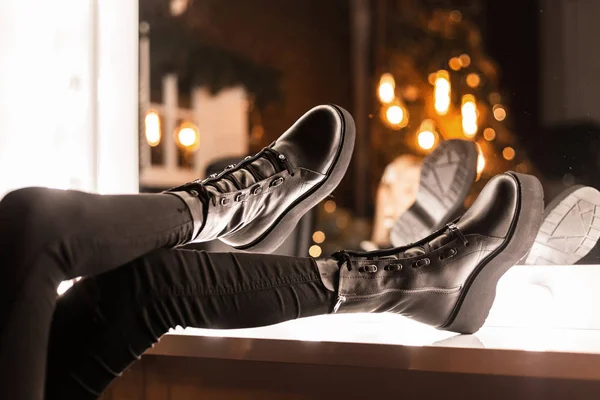 Pernas femininas close-up em jeans pretos em botas de inverno de couro preto na moda perto de um espelho vintage com lâmpadas brilhantes dentro de casa. A rapariga escolhe sapatos para uma festa. Jovens casuais estilo moderno . — Fotografia de Stock