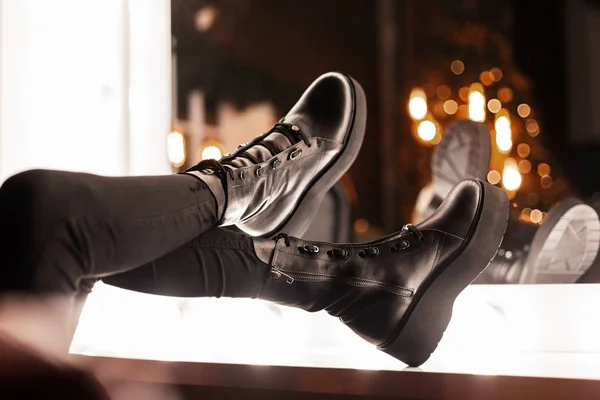 Closeup female legs in black jeans in fashionable black leather winter boots near a vintage mirror with bright light bulbs indoors. Girl chooses shoes for a party. Casual youth modern style. — Stock Photo, Image