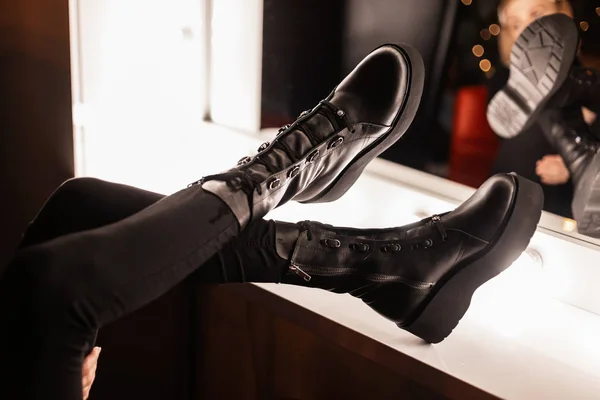 Stílusos fiatal nő divatos fekete gyönyörű bőr cipő divatos farmer közelében egy vintage tükör fényes izzók a szobában. A lány buliba megy. A női lábak közelsége a cipőben. — Stock Fotó