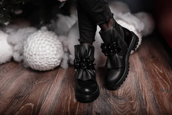 Krásné módní černé kožené boty na ženských nohách uvnitř. Mladá trendy žena ve stylových sezónních botách stojí v místnosti poblíž bílých vinobraných míčků. Nový rok je nakupování. Nová kolekce bot. — Stock fotografie