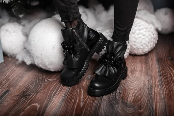 Elegantes hermosas botas de invierno de cuero negro en piernas femeninas cerca de juguetes vintage blancos. Venta de Año Nuevo. Los zapatos a la moda invernales femeninos. Primer plano . — Foto de Stock