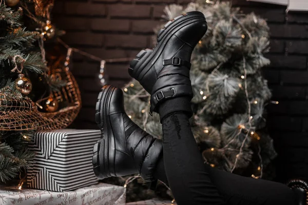 Bottes d'hiver élégantes en cuir noir sur les jambes féminines près d'un beau sapin de Noël festif avec des jouets vintage en studio. Vente de Noël. Chaussures hiver pour femmes à la mode. Gros plan . — Photo