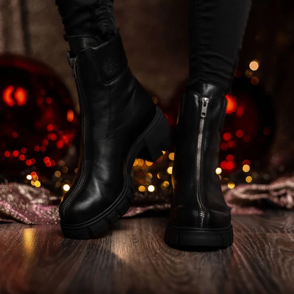 Fashionable leather black women's winter boots. Young woman in jeans in stylish shoes stands in a room near the holiday mirror balls. New Year's shopping. New seasonal shoe collection. — Stock Photo, Image