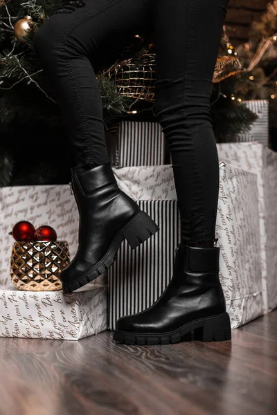 Chaussures de vente de Noël. Collection hiver de chaussures en cuir chaud pour femmes. Gros plan de jambes féminines en bottes noires tendance près des cadeaux de fête et des boules miroir . — Photo