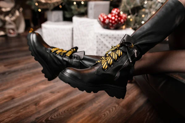 Close-up of female legs in fashionable black leather boots with yellow shoelaces in the studio on the background of gift boxes. New Year's shopping.New collection of women's winter shoes. Winter style — Stock Photo, Image