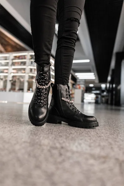 Detailní záběr ženských nohou v módních kožených černých botách ve starých džínách v obchodě. Detaily každodenního vzhledu. Módní podzim-zima. — Stock fotografie
