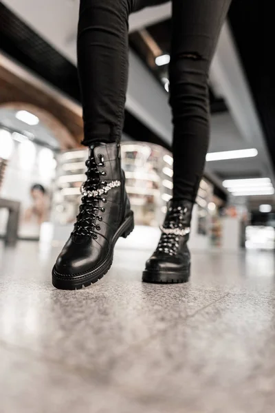 Крупним планом жіночі ноги в чорних модних джинсах в шкіряних чорних стильних мереживних чоботях. Модна жінка позує в торговому центрі. Осіння мода жіноче взуття з блискучими стразами . — стокове фото