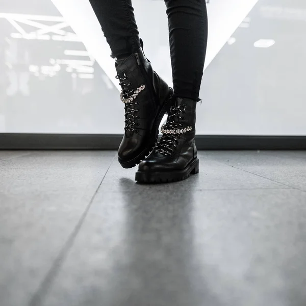 Divatos női szezonális cipők. Új kollekció. Modern fiatal nő elegáns fekete bőr csizma vintage farmer áll egy világos szobában. Női lábak közelsége trendi lábbelikben. — Stock Fotó