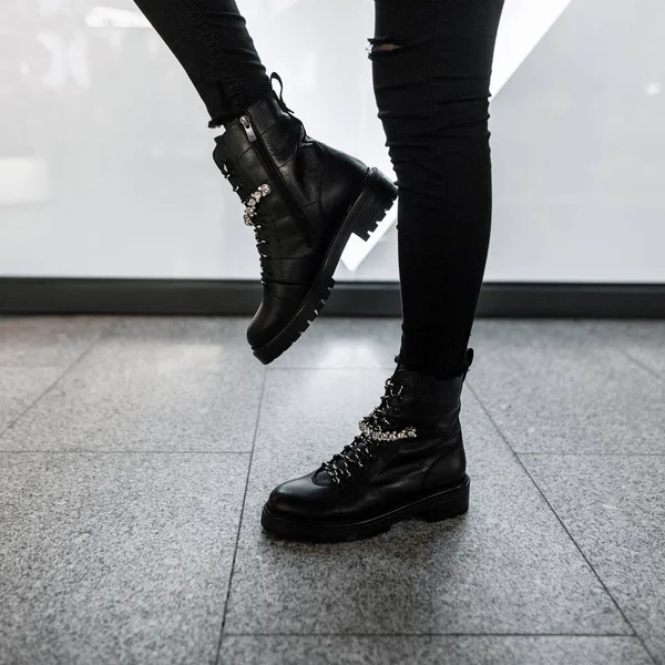 Jeune femme moderne en jeans noirs élégants en cuir à la mode lacets bottes se tient dans un magasin. Collection tendance de chaussures d'automne pour femmes avec strass. Gros plan des jambes féminines dans les chaussures . — Photo