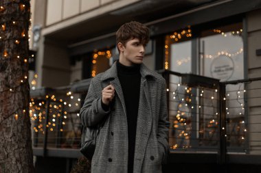 Havalı bir ekose ceketli oldukça yakışıklı bir genç adam modaya uygun bir saç stiline sahip şık bir deri ceketle klasik ışıklı modern bir binanın yanında duruyor. Sokakta yürüyen şehirli adam.