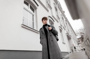Kışlık ekose ceketli, şık, siyah sırt çantalı genç, havalı bir adam bir binanın yanında sokakta yürüyor. Açık havada şık giyinen yakışıklı bir adam. Yeni moda koleksiyonu erkek giyim.