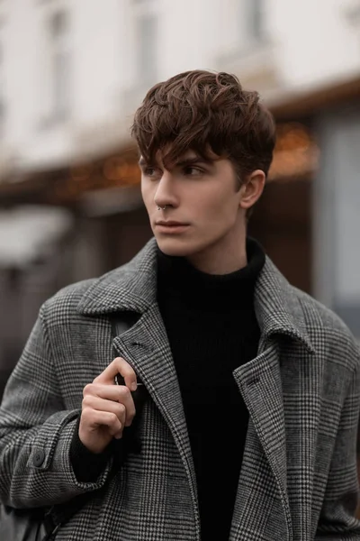 Modèle de mode d'un jeune homme attrayant dans une chemise noire chaude dans un manteau à carreaux à la mode avec un sac à dos en cuir avec une coiffure à la mode. Portrait d'un beau mec en vêtements d'automne élégants . — Photo
