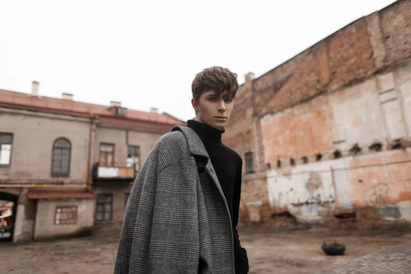 Portrait of a European young man in stylish classic outerwear with a fashionable hairstyle walks along a city street near old buildings. Handsome trendy guy model. Elegant seasonal look. Menswear. — 스톡 사진