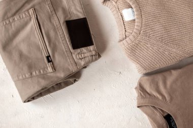 Süslü pamuklu kazaklı, beyaz bir masanın üzerinde yün örülü süveterli şık bej erkek pantolonu. Yeni moda erkek kıyafetleri koleksiyonu. Gençlik tarzı.