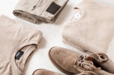 Süet erkek çizmeleri, şık bej süveterler ve beyaz zeminde klasik pantolonlar. Erkekler için pastel renkte moda bahar koleksiyonu. Gençlik çağdaş moda. Retro tarzı. Yakın plan..