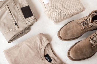 Modern moda erkekler sonbahar-bahar bej süet botları beyaz bir masanın üzerinde şık bir örgü süveter. Erkekler için renkli modaya uygun klasik bir görünüm. Şık sezonluk erkek giyim ve ayakkabıları. Üst görünüm.