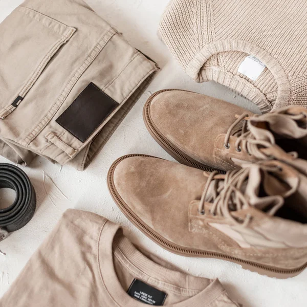 Spring men's clothing style. Trendy beige trousers with fashionable suede boots with a vintage knitted sweater with a classic cotton pullover on a white table. Youth menswear. View from above.Close-up — 스톡 사진
