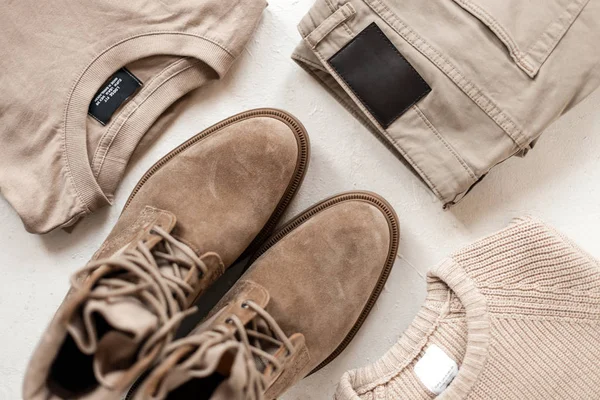 Suede men's fashionable beige boots stand on the white floor next to a knitted sweater with a cotton pullover with classic trendy trousers. Casual stylish look for men. Spring collection. Close-up. — ストック写真