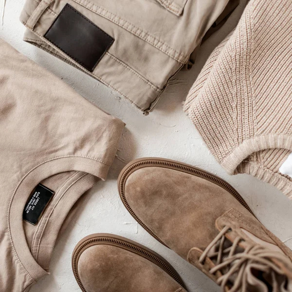 Stylish men's suede boots with fashionable beige casual sweaters with classic trousers on a white table. Trendy spring collection in beige colors for men. Youth modern fashion. Close-up. — ストック写真