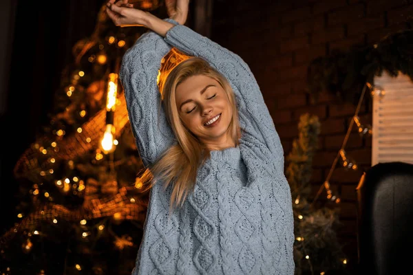 Glamouröse junge Frau in modischem Strickanzug mit blonden Haaren posiert mit geschlossenen Augen in einem Raum mit Weihnachtsbaum. glückliches Mädchen steht und lächelt im Studio mit Neujahrsdekor — Stockfoto