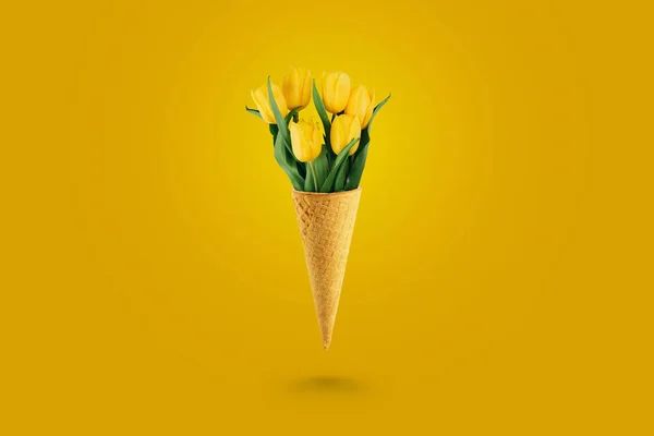 Žluté krásné tulipány v zmrzlině vafle kužel na žlutém pozadí. Konceptuální představa květinového daru. Jarní nálady — Stock fotografie