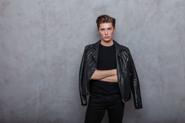 Siyah elbiseli, şık deri ceketli Amerikalı çekici genç adam odadaki klasik gri bir duvarın yanında dinleniyor. Seksi modern moda hippi adam içeride dikiliyor. Moda bakışı..
