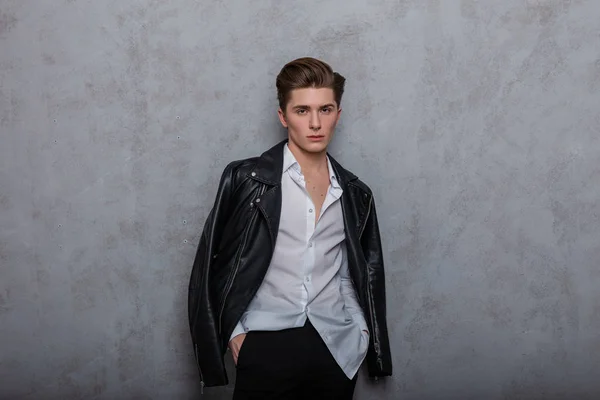 Stüdyodaki klasik gri duvarın yanında siyah beyaz giysili yakışıklı bir adamın seksi mankeni duruyor. Ciddi, zarif hippi, moda saç stili içeride poz veriyor. Biçim.