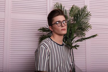 Şık gözlüklü, şık bir genç adam modeli. Odadaki eski pembe ahşap duvarın yanında duran cam bir kapta muhteşem bir çiçek var. Modern hippi adam içeride rahatlıyor..