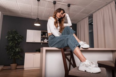 Modayı takip eden kızıl saçlı, modaya uygun genç, mavi-beyaz elbiseli, ahşap bir masada oturan güzel bir kadın. Avrupalı model kız mutfakta dinleniyor. Bayan..