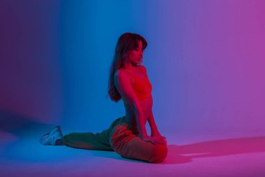 Modern atletik genç bayan moda gençlik kıyafetleri içinde muhteşem mavi bir ışıkla bir odada spor yapıyor. Stüdyoda çok renkli neonlarla yoga egzersizleri yapan sporcu kız..