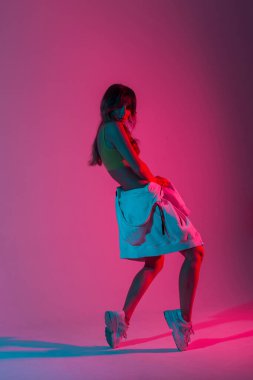 Stüdyoda parlak pembe ultraviyole ışıkla poz veren şık bir kapüşonlu genç bayan dansçı. Modern stil kız disko tarzında neon renkli dans ediyor..