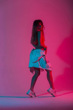 Stüdyoda parlak pembe ışıkla poz veren kapüşonlu, kapüşonlu, güzel bir kadın. Modayı takip eden göz kamaştırıcı kız seksi giyiniyor. Stil diskosunda çok renkli bir renkle iç mekanda duruyor..