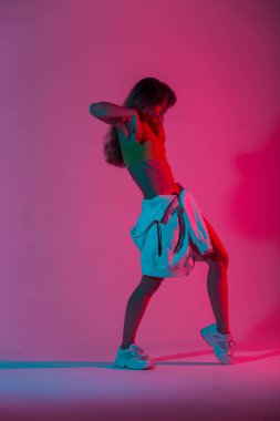 Beyaz spor ayakkabılarıyla kırmızı ışıkta dans eden şık bir genç bayan dansçı. Modern güzel kız model stüdyoda neon pembeli bir dans seviyor. Tarz.