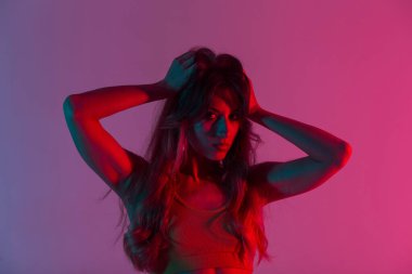 Kapalı mekanda seksi dudakları ve muhteşem pembe ışığı olan şık bluzlu genç bir kadın portresi. Güzel kız manken stil diskosu olan bir odada lüks, uzun saçlar düzleştiriyor..