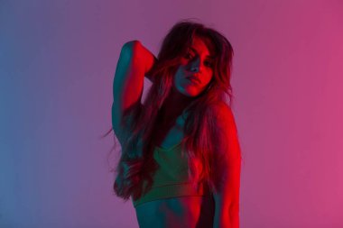 Mükemmel vücudu olan seksi bir bluz giyen, oldukça modern, genç model stil bir kadın uzun saçlarını düzleştiriyor ve parlak neon ışıktan hoşlanıyor. Çok renkli diskosu olan bir odada portre çekici bir kız..