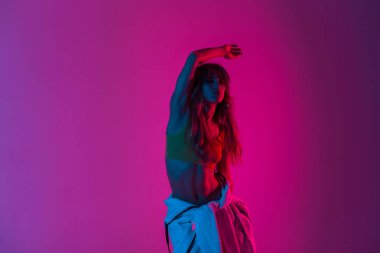 Belinde kapüşonlu bir kapüşonlu genç bayan dansçı açık pembe ışıkla içeride dans ediyor. Uzun saçlı seksi vücutlu sporcu kız disko tarzıyla dans etmeyi seviyor.