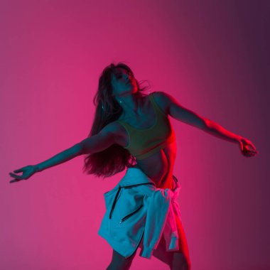 Spor giyim sektöründe şık, genç bir bayan model, rengarenk bir odada dans etmekten zevk alıyor. Parlak pembe neon ışıkla dans eden güzel seksi kız..