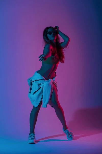明るいネオンブルーピンク色の部屋で踊るジムの靴のサングラスでスタイリッシュな若い女性ダンサー 女の子のヒップスターは 多色の紫外線光とスタジオでダンスを楽しんでいます — ストック写真