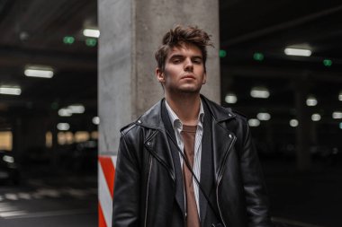 Kentin bir caddesinde, modaya uygun saç stili olan klasik gömlekli, siyah ceketli Avrupalı genç bir adam duruyor. Yakışıklı, modacı, açık havada manken. Erkekler için gençlik kıyafetleri.