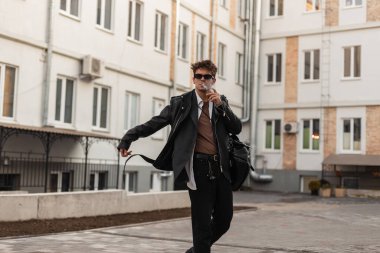 Moda gözlüklü, deri ceketli, sırt çantalı ve klasik binaların yanında sigara içen genç hippi. Büyük beden elbiseli modacı adam sigara içmekten hoşlanıyor..