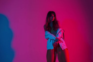 Modern manken, şık genç elbiseli güzel güzel bir kadın göz kamaştırıcı pembe bir ışıkla bir odada duruyor. Stüdyoda neon renkli pozlar veren modacı kız..