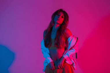 Disko tarzında pembe ve mavi renkli bir odada poz veren moda gençliği kıyafetleri içinde oldukça seksi genç bir kadın. Güzel, şehvetli kız stüdyoda çok renkli, şık bir ışıkla bekliyor..