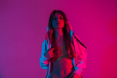 Moda mankeni şık genç elbiseli güzel bir kadın göz kamaştırıcı bir pembe ışıkla bir odada duruyor. Modern moda kızı stüdyoda neon renkli simlerle poz veriyor.