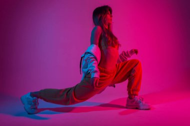 Havalı genç bayan dansçı dans etmeden önce fitness yapıyor. Stüdyoda parlak mavi-pembe ışıkla poz veren şık spor elbiseli çekici bir kız. Bayan ve neon.