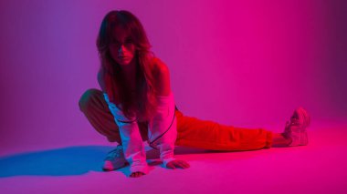 Şık spor kıyafetleri ve ayakkabıları olan seksi, modern bir kadın parlak pembe renkli bir moda stüdyosunda esneme hareketleri yapıyor. Güzel atletik kız dansçı içeride neon ışıkla spor yapıyor..