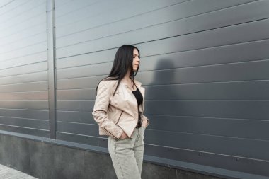 Şık kotlu, büyük beden deri ceketli, şık, kentli genç bir kadın şehrin klasik binasının yanında yürüyor. Moda kıyafetleri içinde moda bir kız dışarıda dolaşıyor. Sokak gündelik tarzı