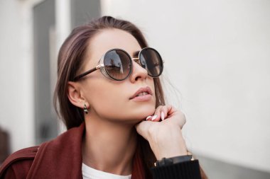 Moda tarzı koyu güneş gözlüklü, açık havada şık kahverengi pelerinli güzel hippi kadın portresi. Sokakta seksi dudakları olan temiz tenli çekici bir manken kız. Yakın plan.